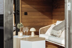 A cozy room with wooden walls, a white sofa, a small table with a plant, two glasses, and a decorative lamp. - l'empreinte (Verzenay)