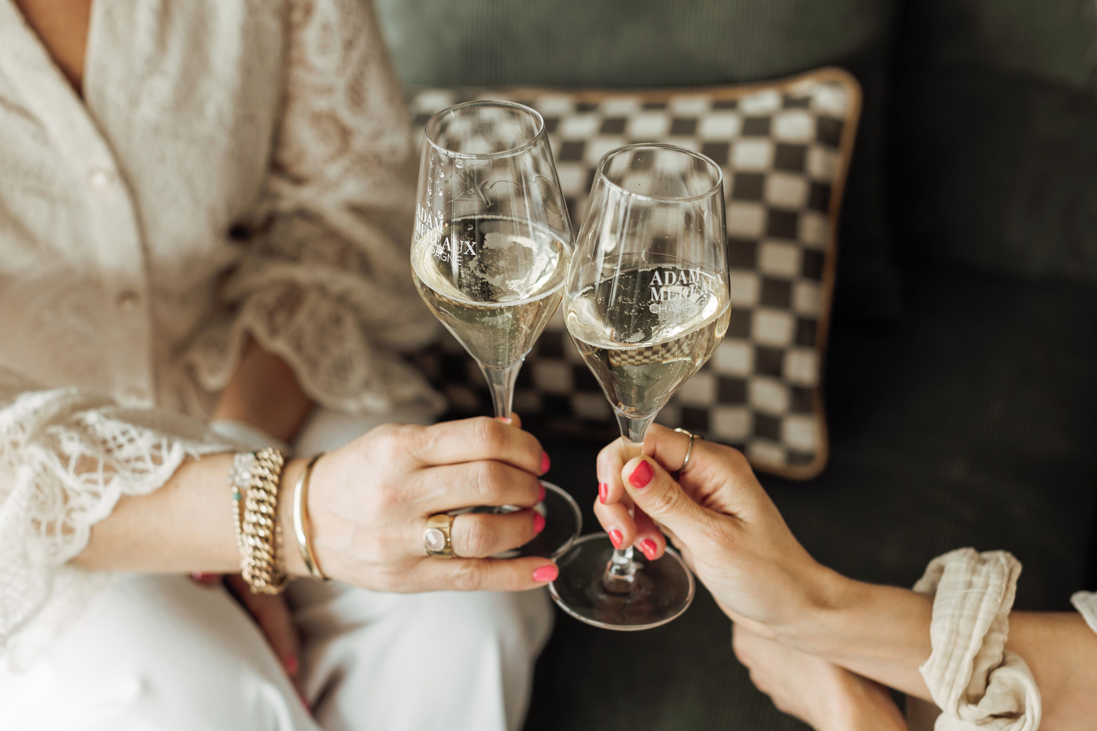 Two people holding champagne glasses with the text "ADAM M" on them, seated on a couch with a checkered pillow in the background.