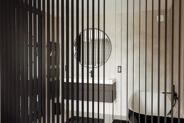 A modern bathroom with a black and white color scheme, featuring a round mirror, a sink, and a bathtub. - l'empreinte (Verzenay)