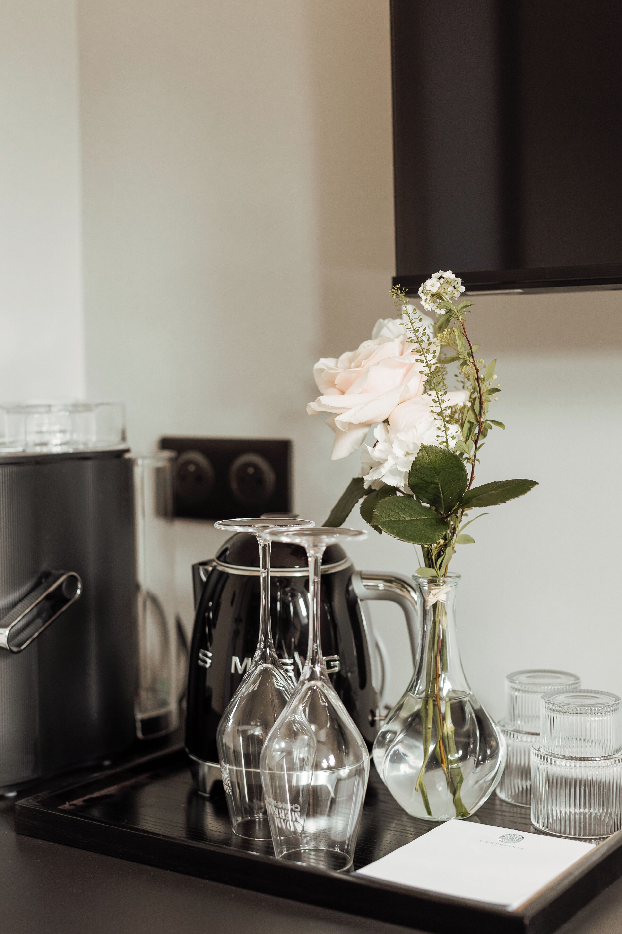 A kitchen counter with a coffee maker, a vase with flowers, and several glasses.