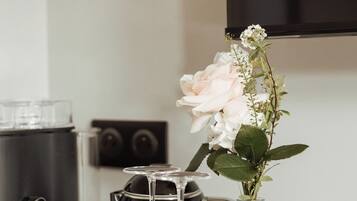 A kitchen counter with a coffee maker, a vase with flowers, and several glasses.