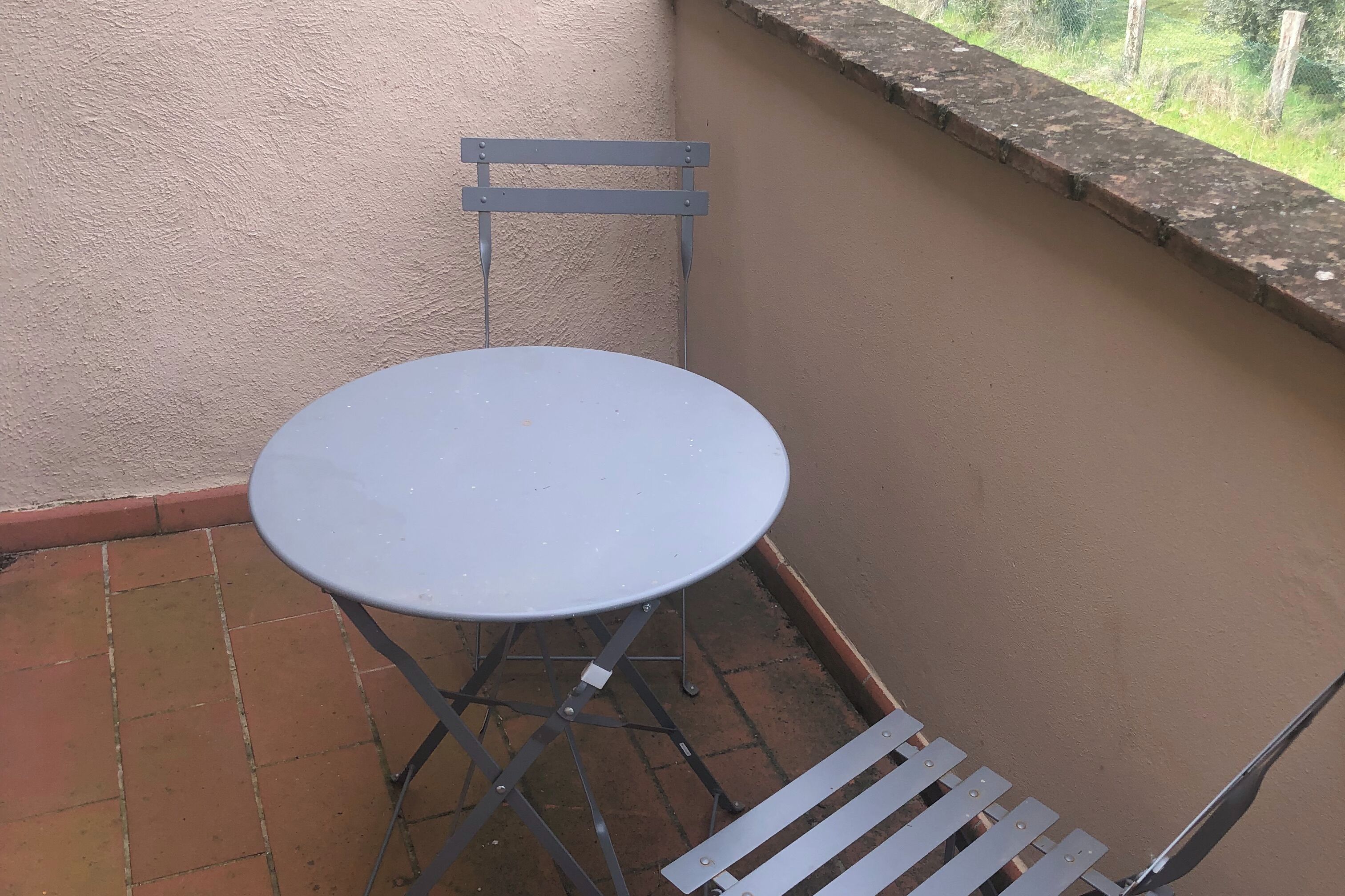 Un pequeño balcón exterior con una mesa redonda de metal y una silla.