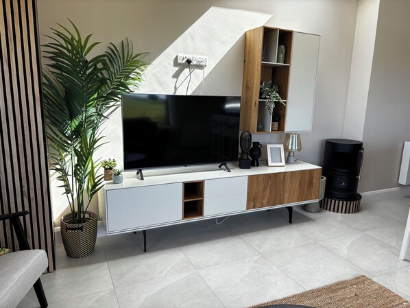 A modern living room with a flat-screen TV, wooden and white cabinetry, a potted plant, and a black speaker.