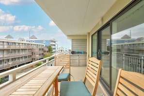 A balcony with wooden furniture, a view of a building with multiple windows, and a clear sky. - Salty Sands 306 by Seaside Vacations & Sales (Ocean City)