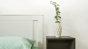 A bed with green bedding, a white vase with a plant, and a dark-colored nightstand with a magazine. - VACATION HOME EL'GIO HOME PORDENONE (Pordenone)