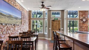 Un restaurant aux murs de pierre, aux tables et chaises en bois, doté d’un bar et de grandes fenêtres offrant une vue sur l’extérieur.