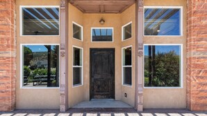 Une entrée d’immeuble avec une porte en bois foncé, de grandes fenêtres et une façade en briques.