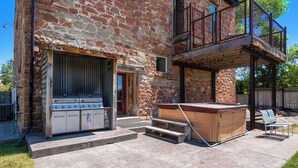 Un bâtiment en pierre doté d’un espace barbecue, d’un jacuzzi et de coins salon extérieurs.