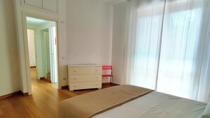 Um quarto com cama, cômoda e porta que dá para outro espaço.