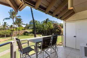 A covered outdoor seating area with a table and chairs, overlooking a landscaped garden with palm trees and a golf course.