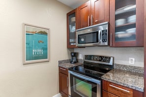 A kitchen with wooden cabinets, a stainless steel microwave, a stove, and a coffee maker.