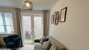 A modern living room with a sofa, a blue armchair, a round rug, and a dining area visible through glass doors. - Captivating 2-bed Cottage in Symonds Yat (Ross-on-Wye)