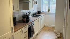 A modern kitchen with white cabinets, a wooden countertop, and a window with blinds. - Captivating 2-bed Cottage in Symonds Yat (Ross-on-Wye)