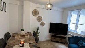 A modern living room with a dining area, a flat-screen TV, and a blue armchair. - Captivating 2-bed Cottage in Symonds Yat (Ross-on-Wye)