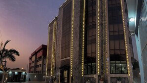A modern building with vertical light strips along the facade, large windows, and a palm tree in the foreground. - Mini Palace Luxury Suites (Abuja)