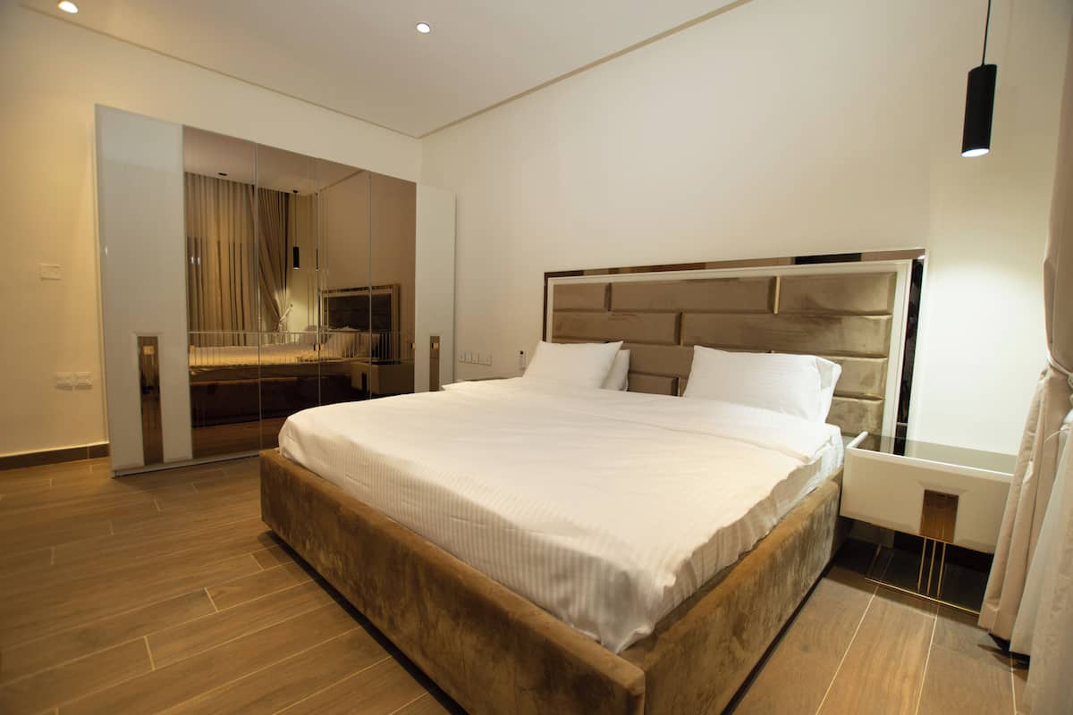 A modern bedroom with a large bed, a mirror, and a walk-in closet.