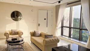 A modern living room with a beige sofa, a round coffee table, and a large window with curtains. - Mini Palace Luxury Suites (Abuja)