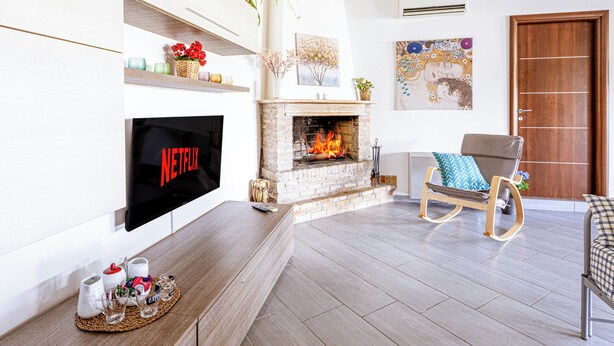 Ein modernes Wohnzimmer mit Kamin, einem Flachbildfernseher, der 'NETFLIX' anzeigt, und einer gemütlichen Sitzecke mit Schaukelstuhl und Sesseln.