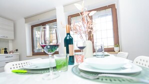 Ein Esstisch mit Tellern, Gläsern und einer Flasche, in einem Raum mit großen Fenstern und heller Einrichtung.