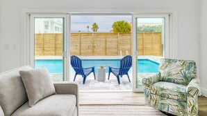 A living room with a pool view, a grey sofa, blue chairs, and a tropical-patterned armchair. - Sweetwater Sunrise (St. Augustine)