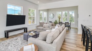 A spacious living room with a large sectional sofa, a flat-screen TV, and a dining area with a table and chairs. - Sweetwater Sunrise (St. Augustine)