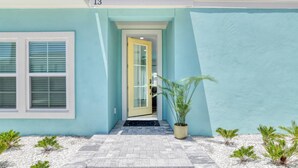 A building with a light blue exterior, a number '13' above the entrance, a glass door, and a small potted plant in the foreground. - Sweetwater Sunrise (St. Augustine)