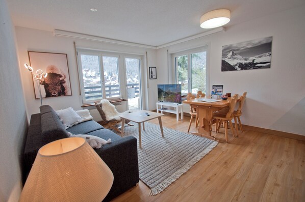 Relax in this stylish living room with a sofa, coffee table, and dining table, offering a view of the surrounding landscape.