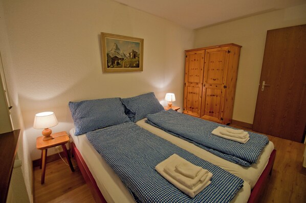 Un dormitorio con dos camas, un armario de madera, un cuadro en la pared y una mesita de noche con una lámpara.