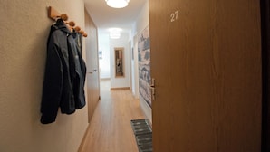 A hallway with wooden walls, a coat rack with jackets, a door labeled '27', and a light fixture on the ceiling.