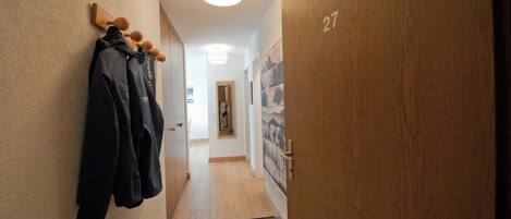 A hallway with wooden walls, a coat rack with jackets, a door labeled '27', and a light fixture on the ceiling.
