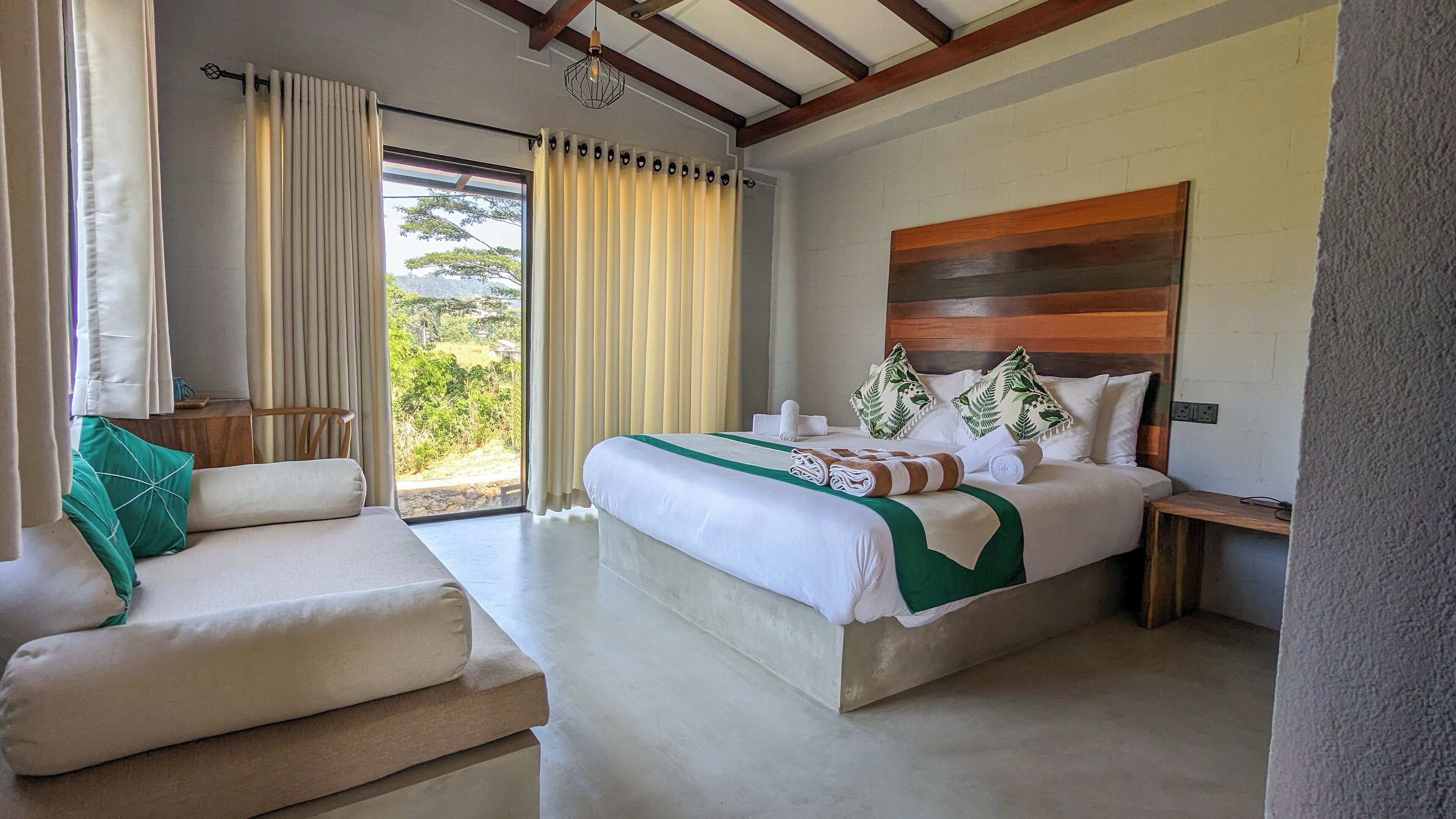 Un dormitorio con cama, sofá, mesita de noche y vistas al exterior.