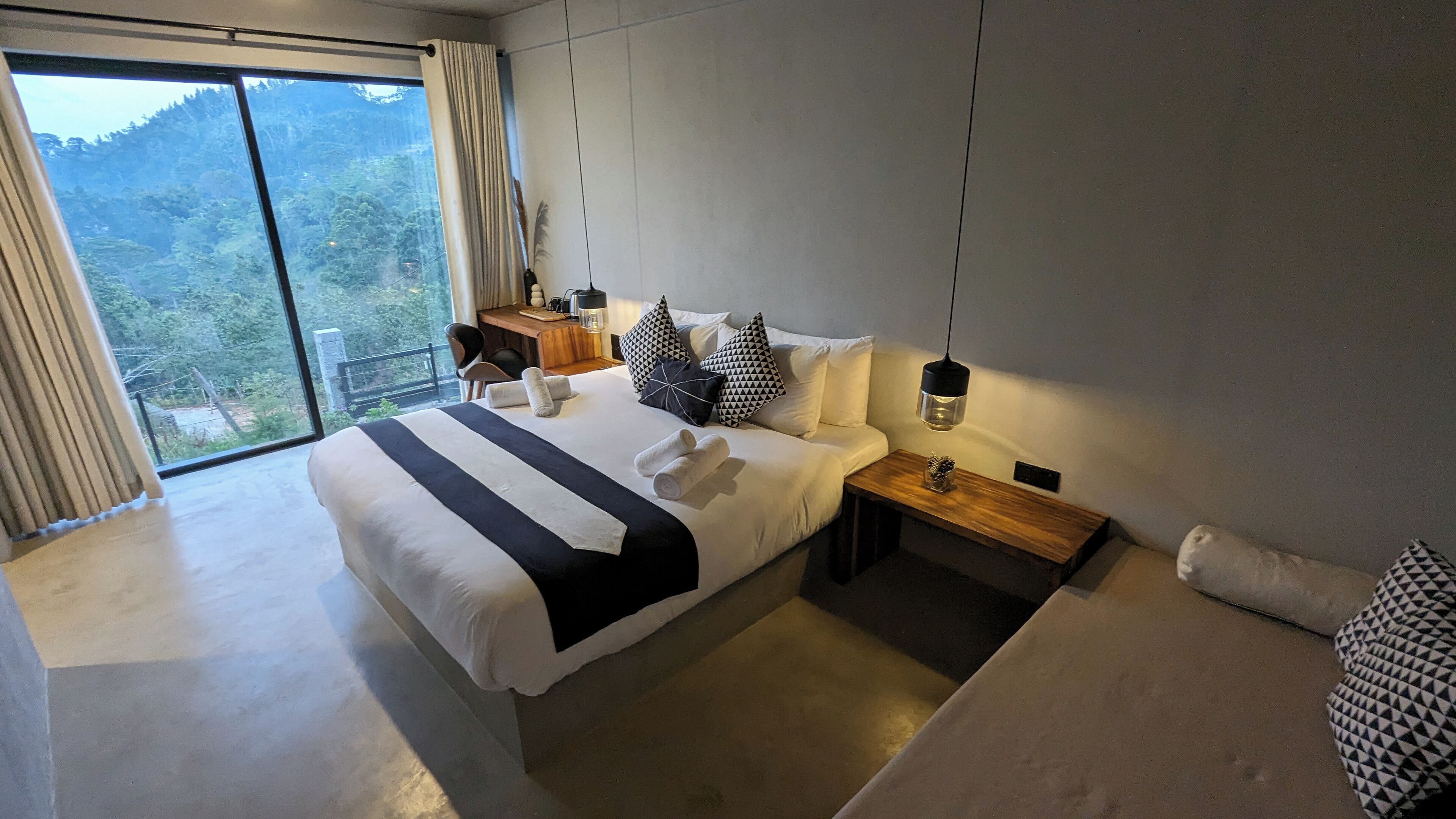 Una habitación de hotel moderna con una cama grande, una mesita de noche de madera y vistas al exterior.