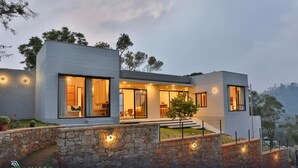 Une villa moderne dotée de grandes fenêtres, d’une façade en pierre et d’un intérieur bien éclairé.