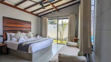 A bedroom with a large bed, wooden headboard, and a view of a garden through a sliding glass door.