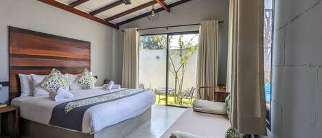Un dormitorio con una cama grande, cabecera de madera y vistas a un jardín a través de una puerta corrediza de vidrio.