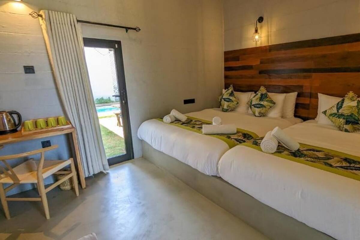 Een tweepersoonskamer met twee bedden, een houten hoofdbord, een kleintje tafeltje met kopjes, en uitzicht op de omgeving.