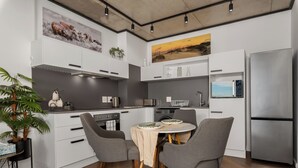 Une cuisine moderne avec des meubles blancs, un réfrigérateur en acier inoxydable et un coin repas comprenant deux chaises grises et une table.