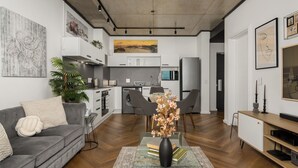 Un salon moderne avec un canapé gris, une table basse agrémentée de livres et d’un vase, un coin repas avec des chaises, et une cuisine en arrière-plan.