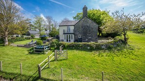 A stone house with a balcony, surrounded by a well-maintained lawn and a wooden fence. - Luxurious Three Bedroom Farmhouse with Sea Views in Llanystumdwy | Bryn-Du (Criccieth)