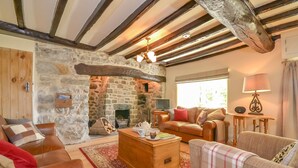 A cozy living room with a stone fireplace, wooden beams, leather sofas, and a wooden coffee table. - Luxurious Three Bedroom Farmhouse with Sea Views in Llanystumdwy | Bryn-Du (Criccieth)