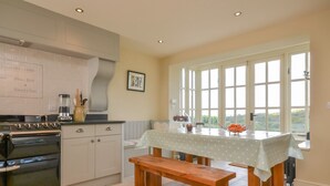 A kitchen with a wooden bench, a table with a polka dot tablecloth, and a view through large windows. - Luxurious Three Bedroom Farmhouse with Sea Views in Llanystumdwy | Bryn-Du (Criccieth)