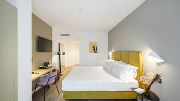 Camera d'albergo con un letto, una scrivania, una sedia, una TV e una lampada a parete.