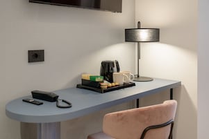Una camera d'albergo moderna con una scrivania, una lampada, una macchina del caffè e una sedia.