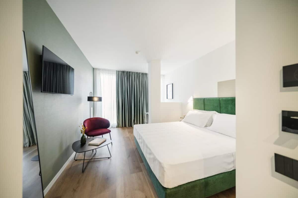 Quarto de hotel moderno com uma cama grande, uma cadeira vermelha, uma televisão de tela plana e um abajur.