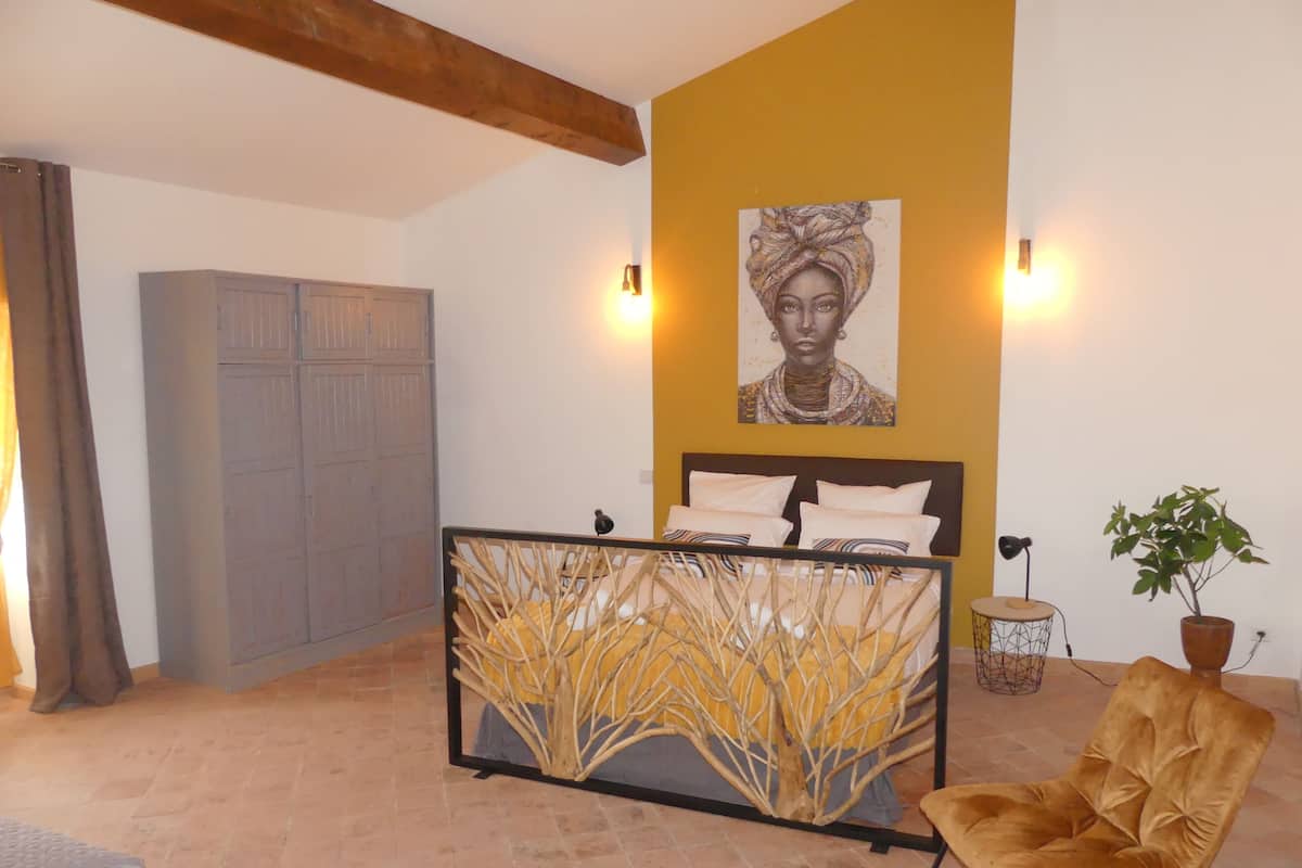 A bedroom with a bed, a chair, a plant, and a painting on the wall.