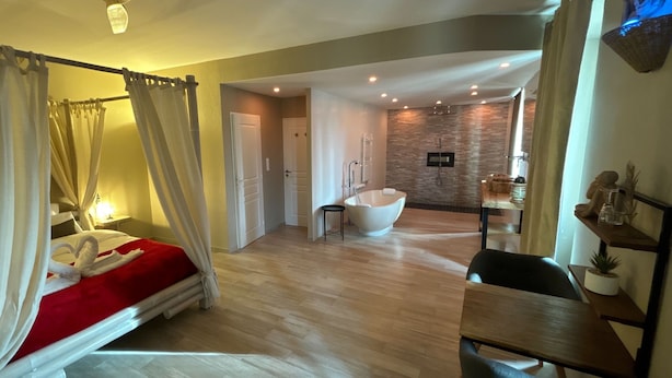 Un dormitorio amplio con cama con dosel, baño independiente con bañera y un comedor.