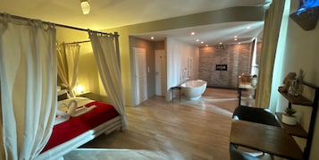 Un dormitorio amplio con cama con dosel, baño independiente con bañera y un comedor.