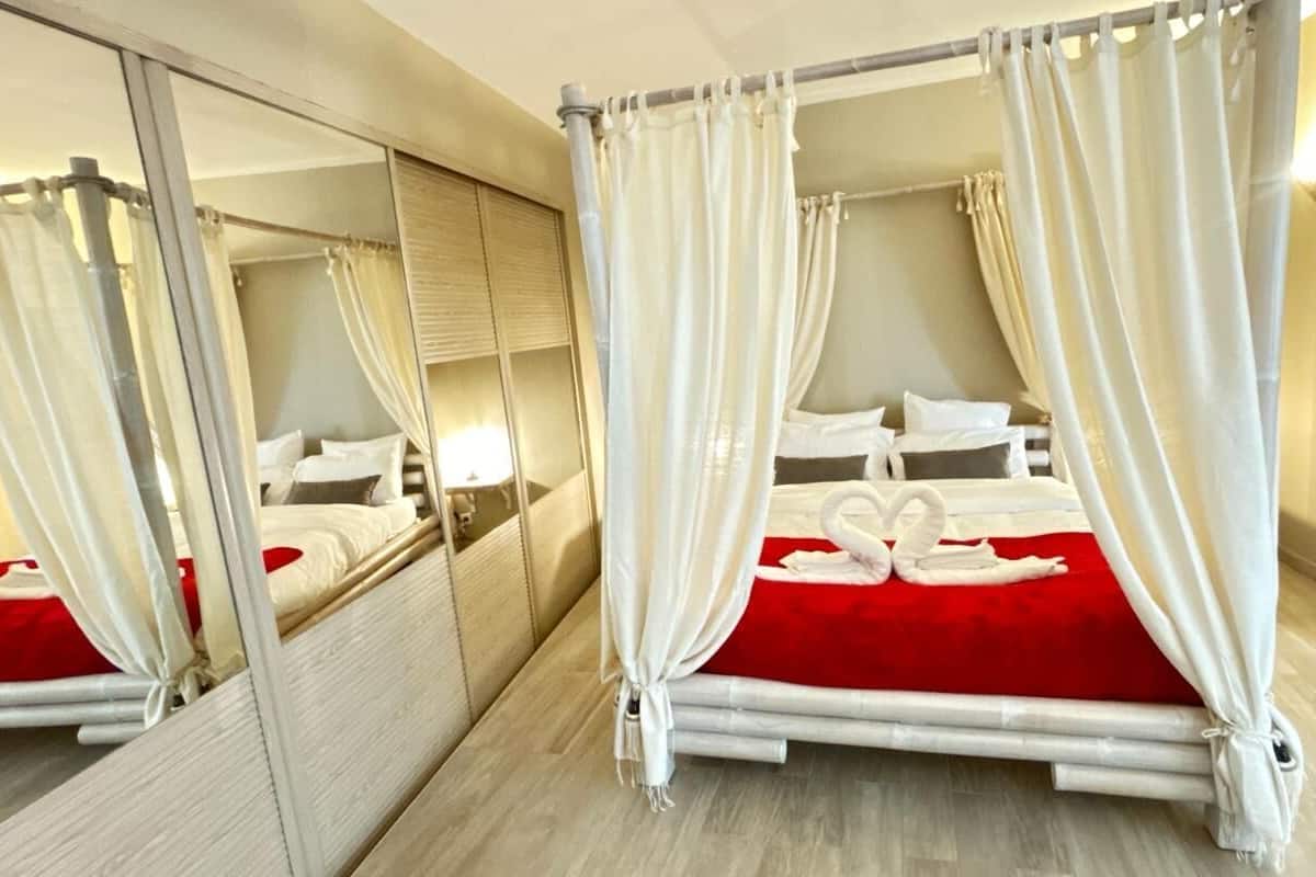 A double room with a mirrored wardrobe, a red bedspread, and a swan-shaped towel decoration.