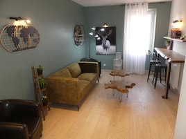 Una sala de estar con sofá, mesa de centro y sillas. Hay un comedor con mesa y sillas. La habitación tiene un mapa mundial y un cuadro de un ciervo en la pared.