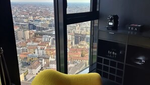 Ein Hotelzimmer in einem Hochhaus mit gelbem Sessel, Kaffeemaschine und Blick auf die Stadtlandschaft.